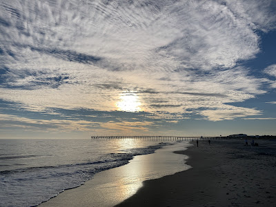 A random picture of the sky and the ocean. The sky it dotted with light clouds as the sun is beginning its descent over the horizon.