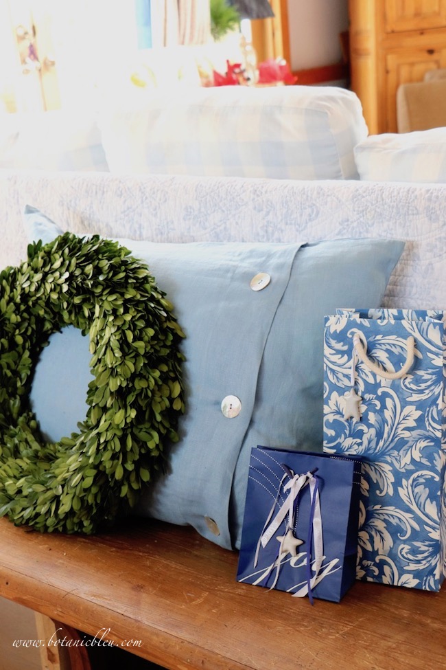 Blue and white Christmas packages with a large blue linen pillow and boxwood wreath sit on a vintage church pew.