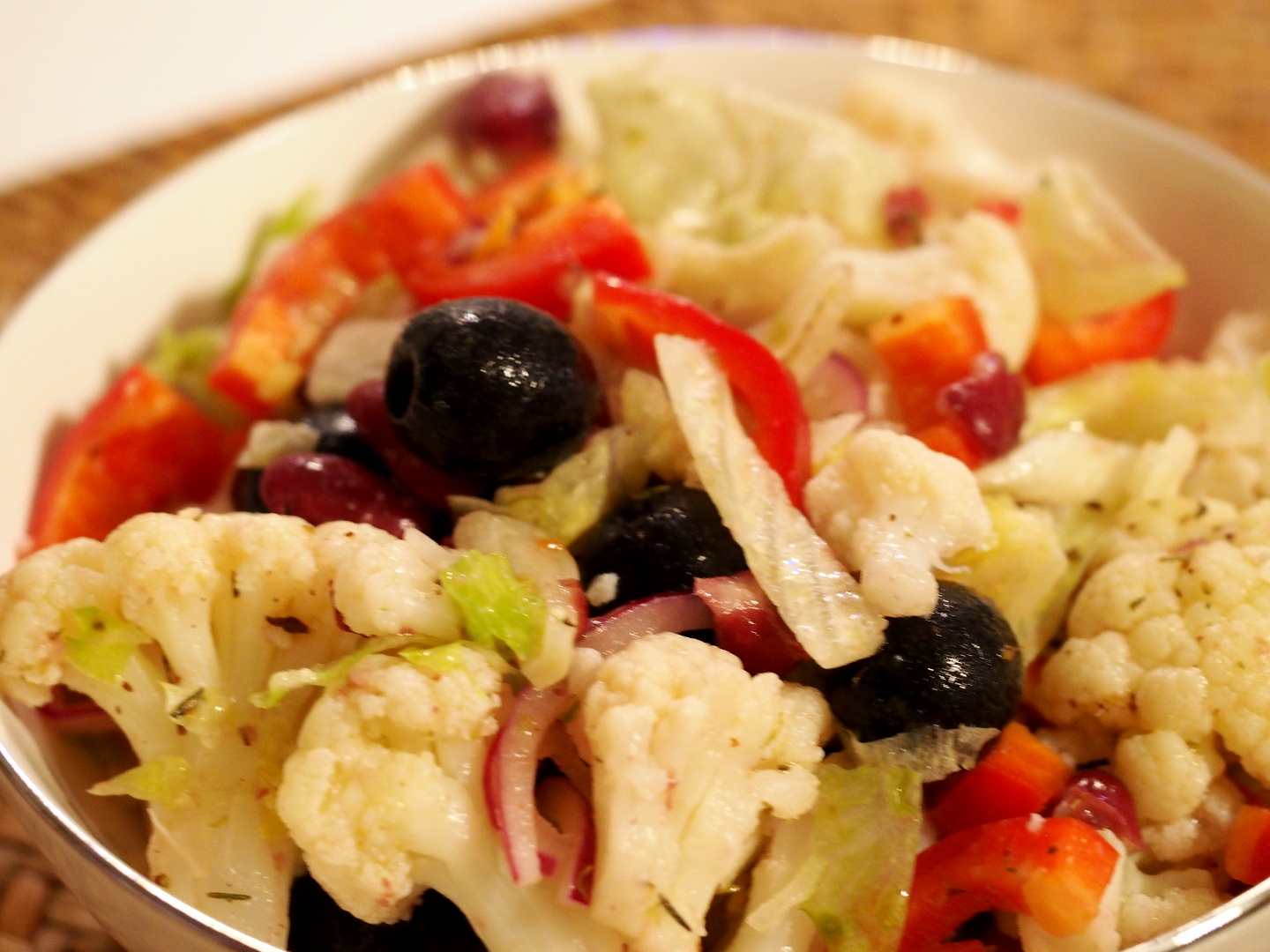 Eine Schüssel gefüllt mit dem Salat aus Blumenkohl, Paparika, Eisbergsalat und schwarzen Oliven