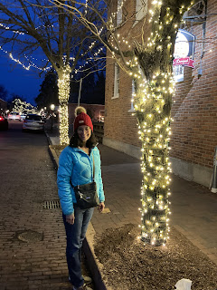 Woman standing in front of trees wrapped in Christmas lights 