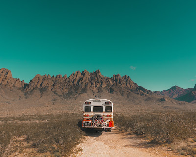 back of red and white bus parked on a dirt road with mountains and blue sky in the background