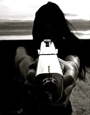 Long haired brunette backlit pointing a gun at the camera her face is impossible to see