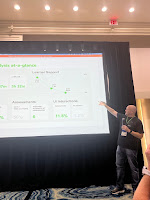 A man standing in front of projected screen share, pointing at numbers on a mocked up data dashboard.