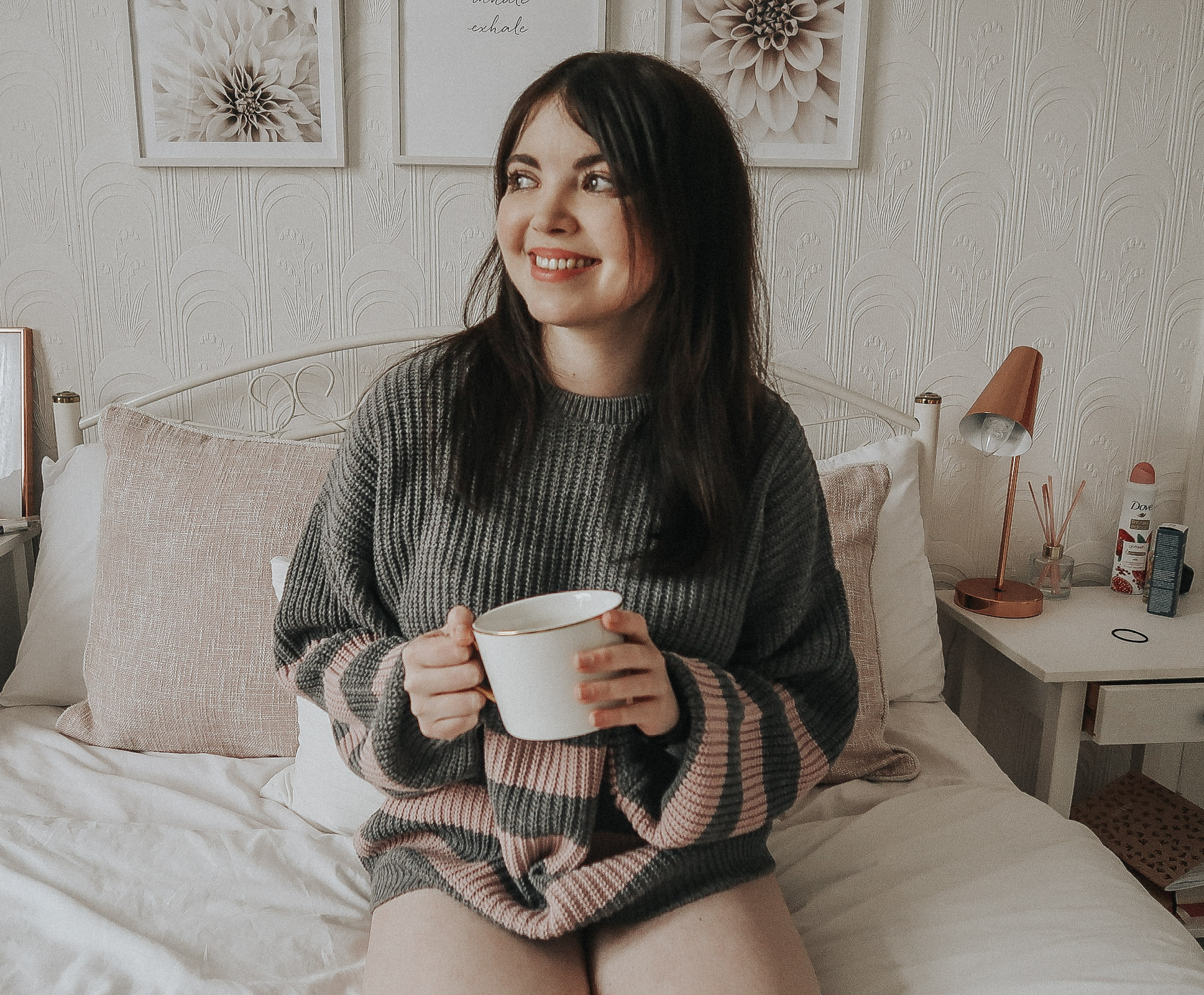 A woman wearing a grey and white jumper holding a white mug.