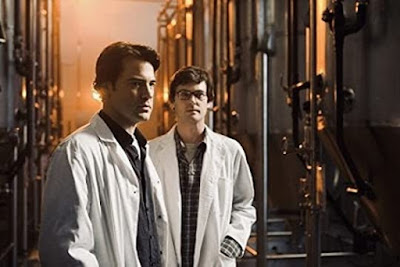 Ron Livingston and Henry Thomas standing in front of large lab mixing equipment