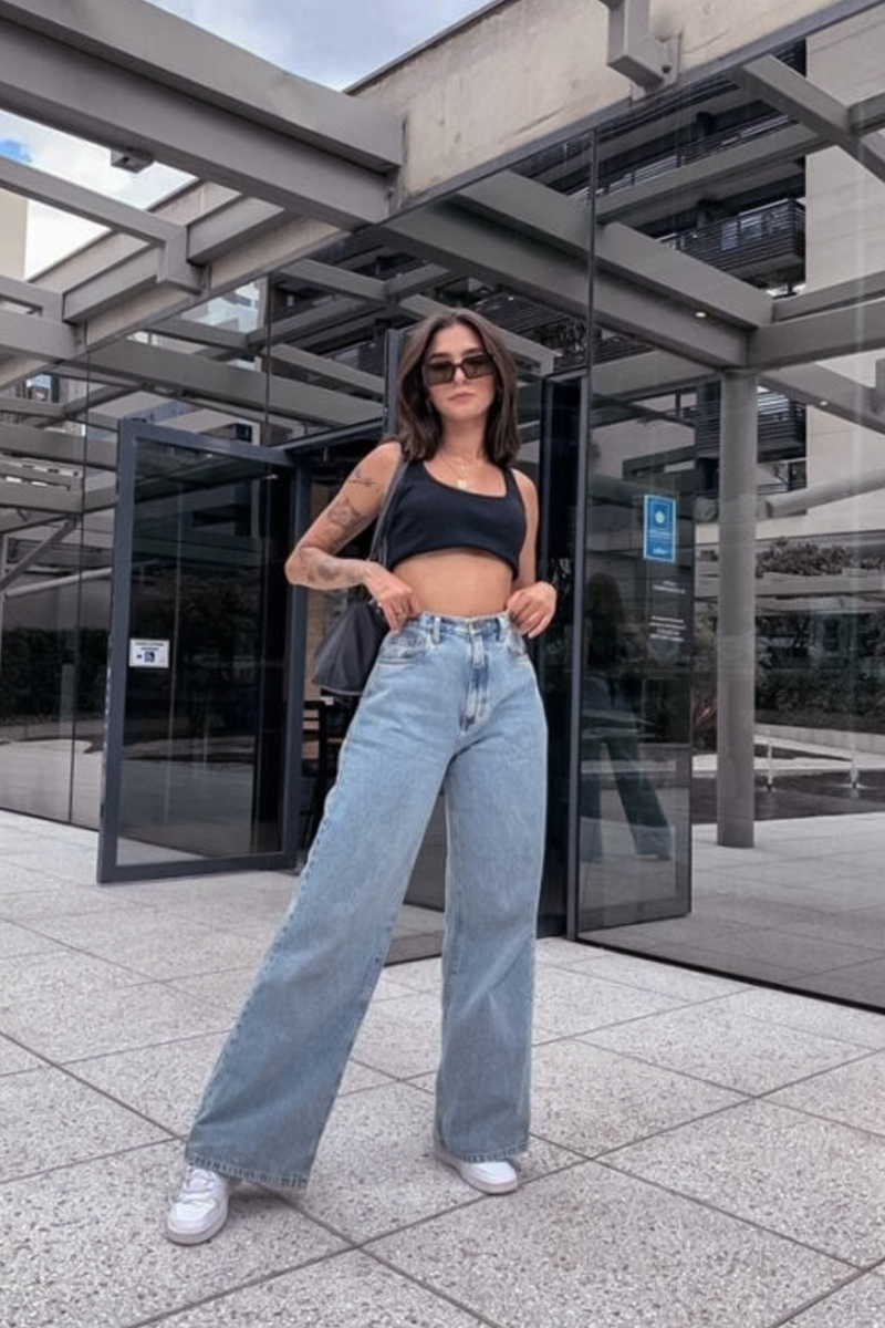 beautiful woman in wide leg jeans and crop top is posing on a street