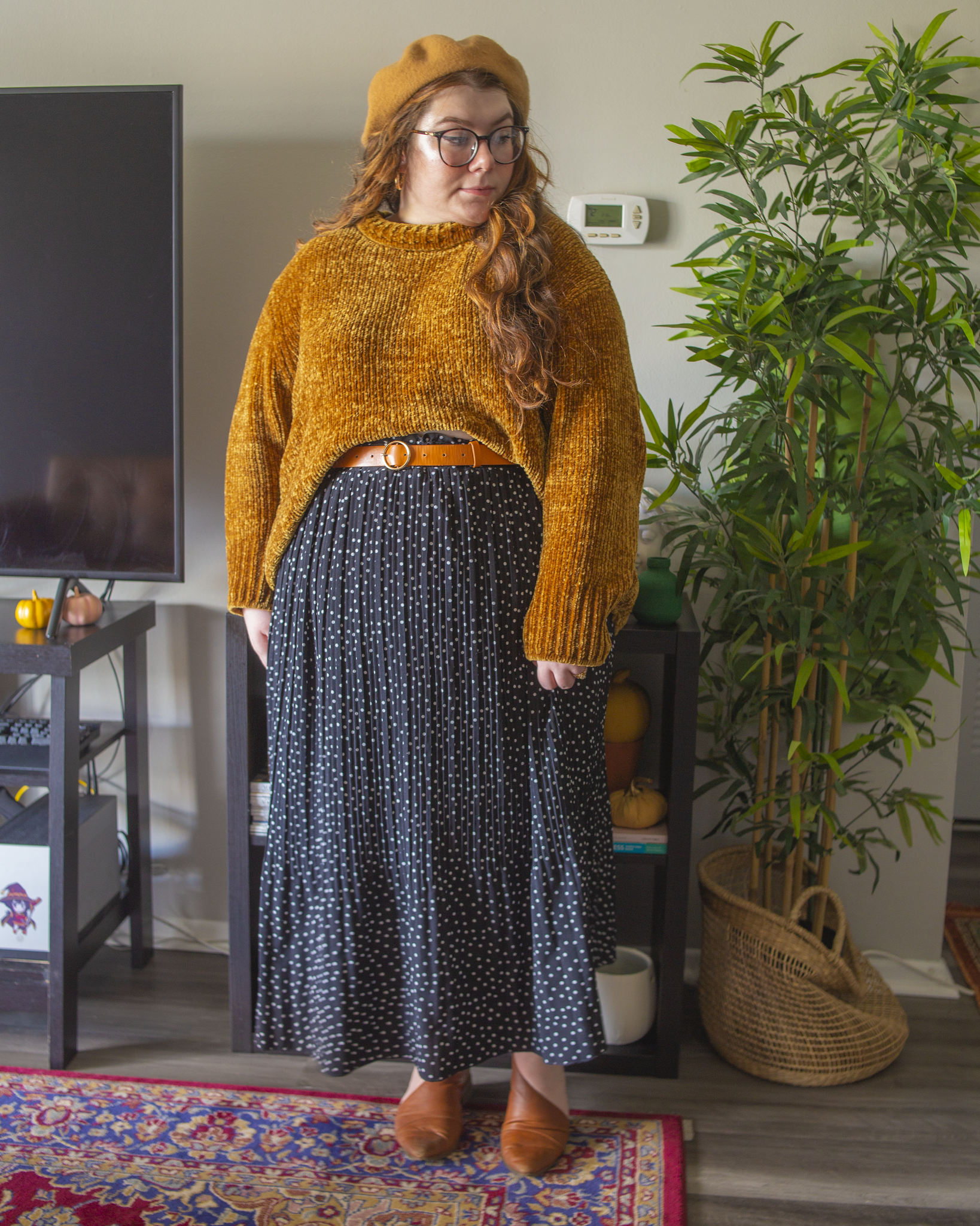 An outfit consisting of a yellow chenille sweater half tucked into a white on black micro swiss dot midi skirt and black Chelsea boots.