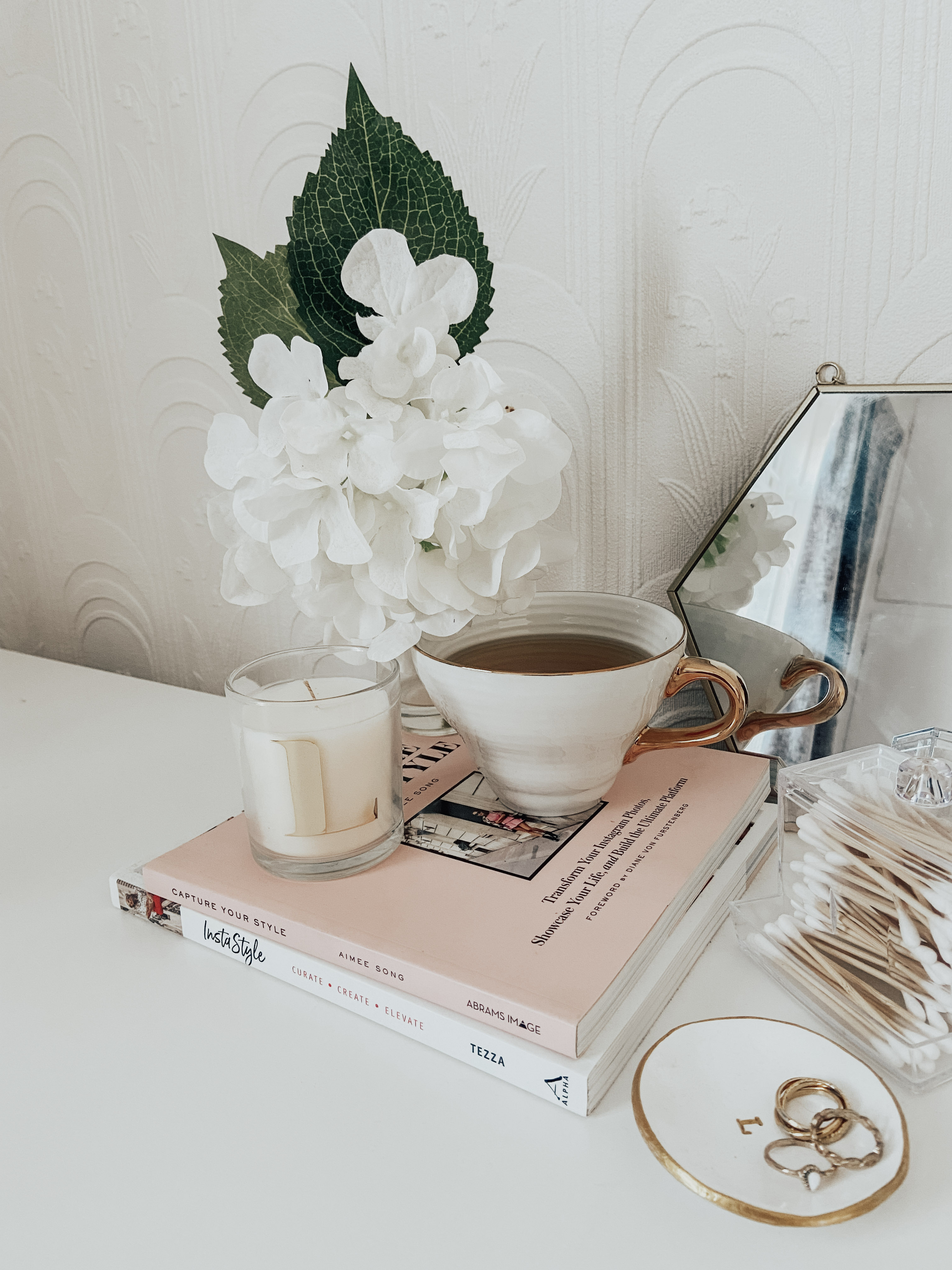 A white mug, a white artificial plant on top of pink books.