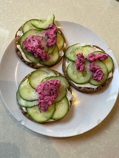 A plate of three rye bread crackers, spread with cream cheese and topped with sliced cucumber and a dollop of beetroot salad.