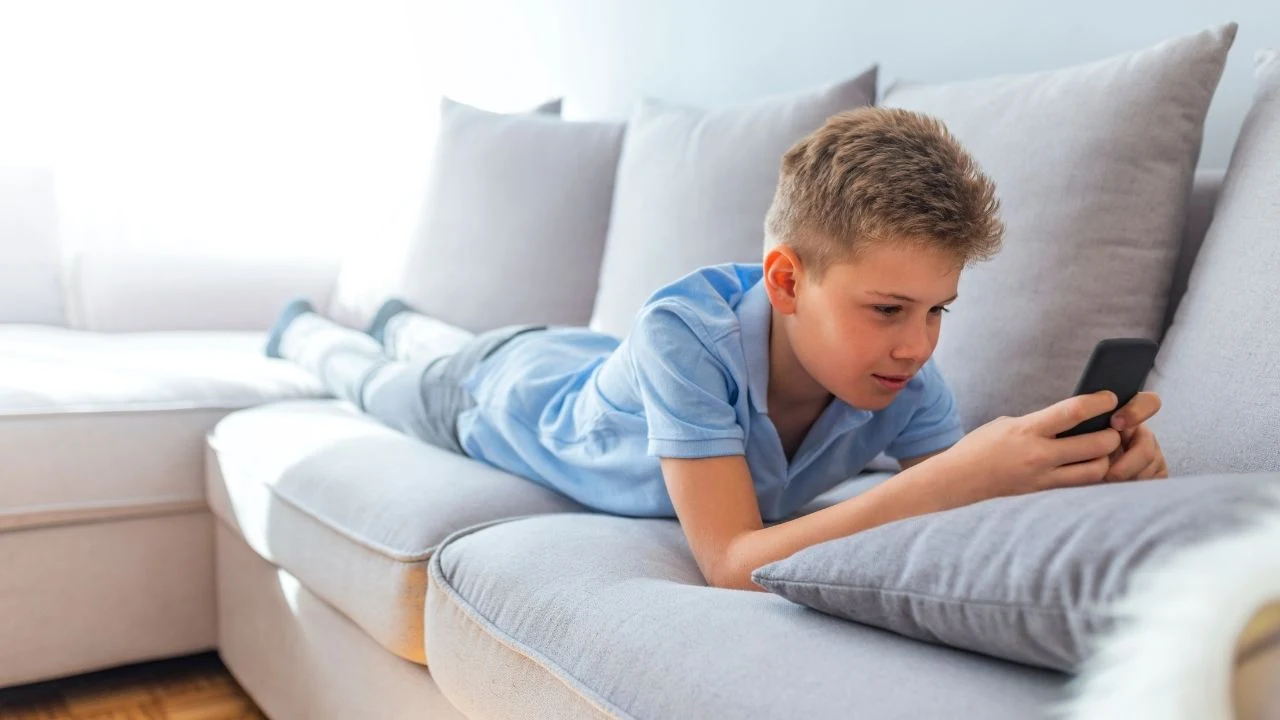 Internet and social networks for teenagers, boy concentrated on phone, laying on front of sofa.