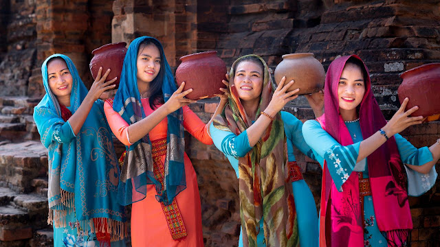 A group of women are holding pots in front of a brick wall.