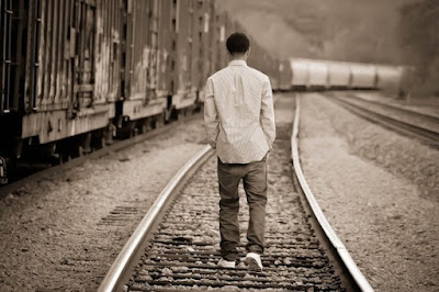 black and white image of young man walking on railroad