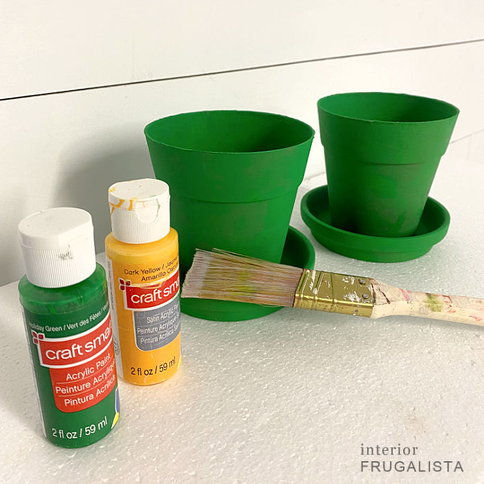 Painting small flower pots green to make a leprechaun hat craft for St. Patrick's Day.