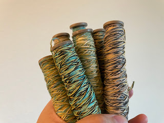 A hand holding boat shuttle bobbins, with colorful cotton yarn wound on.