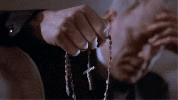 Max von Sydow holding his head in one hand and a rosary in the other