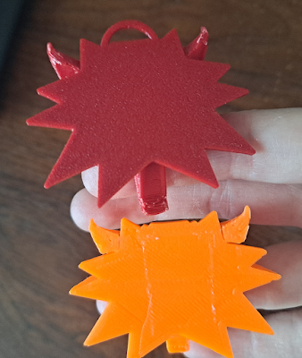 The bottom sides of the two amulets. Red (Vyper-printed) amulet has a very even surface with a regular marbled texture on it. Bottom amulet (printed on tape) has traditional smushed diagonal lines plus some irregularities from boundaries between tape strips.