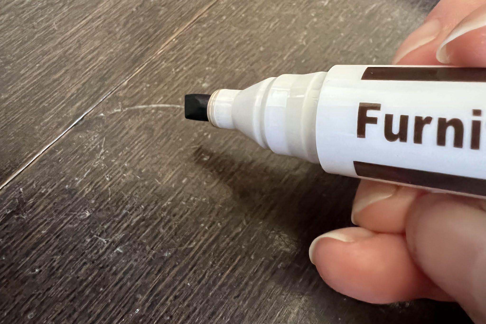 A close up of a wooden furniture repair pen next to a scratch on dark wood floor