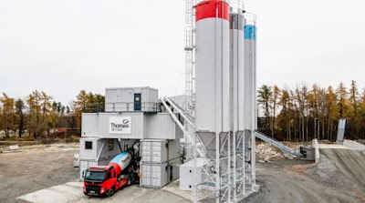 Bild på betongfabrik med höga silos och betongbil som lastar.