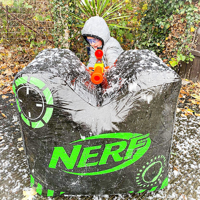 Little boy crouched behind an inflatable crate with a sniper Nerf gun