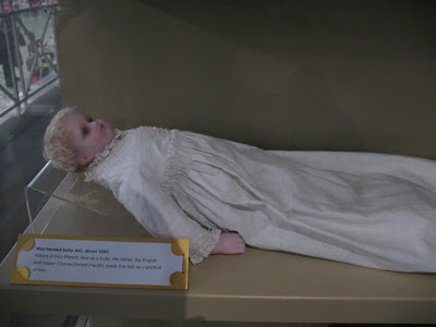 Doll; a baby dressed in a white nightgown, laying as if in bed