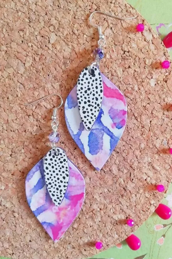 double modified oval dangle earrings with purple/pink watercolor print and dotted black/white paper designs displayed on cork board