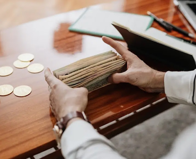 Manos de persona de espaldas, con billetes y monedas sobre un mostrador