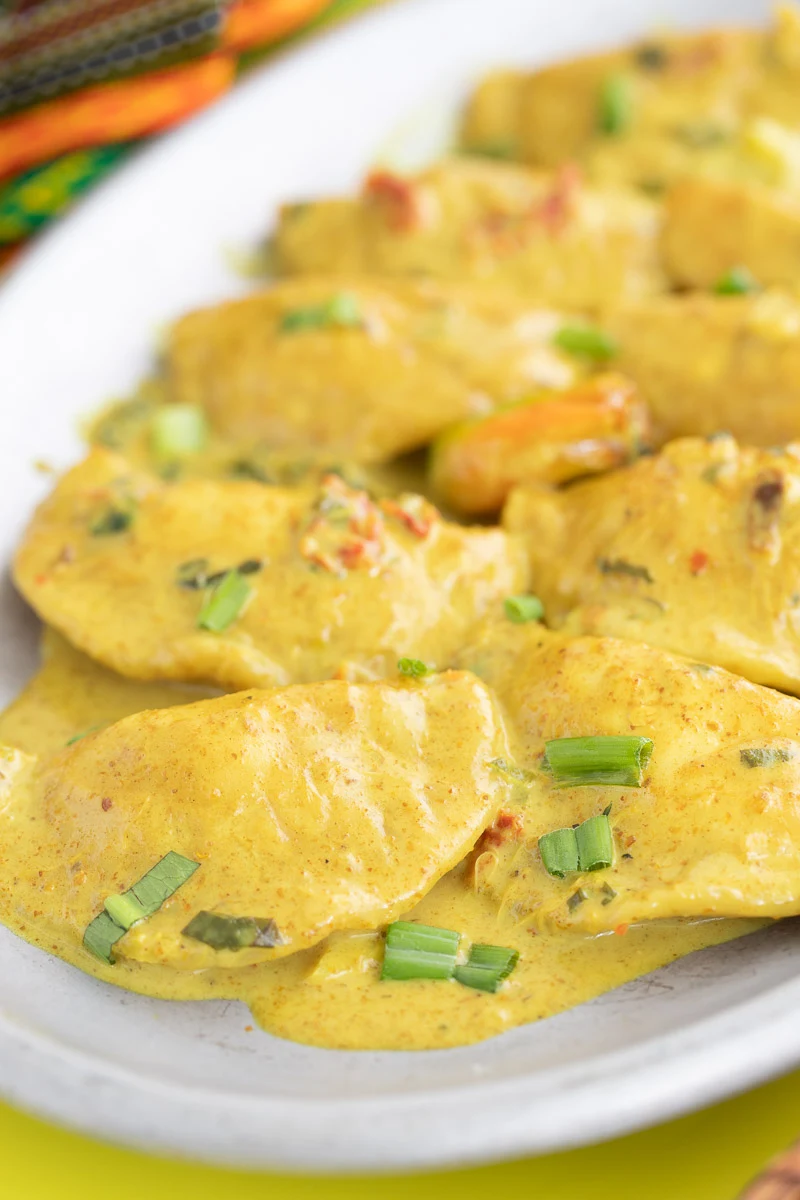 Dumplings in coconut curry sauce in a metal grey plate, garnished with scallion, ready to be served.