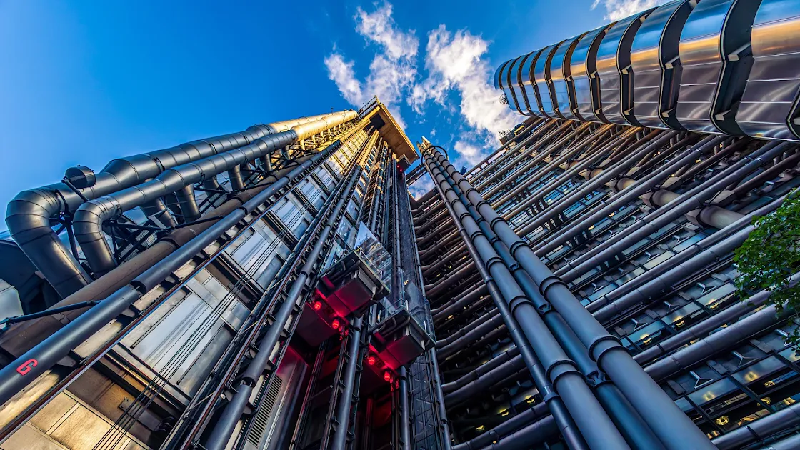 Upward view of a modern skyscraper's intricate steel exterior with exposed pipes against a clear blue sky in 4K resolution.