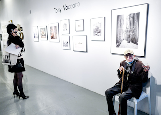 99-year old Tony Vaccaro sitting by his photographs with a glass of wine