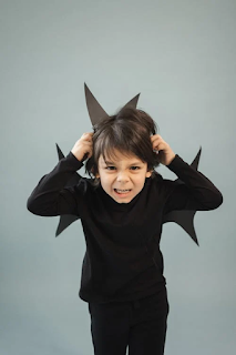 A young child dressed as a devil, making a playful grimace in a studio setting
