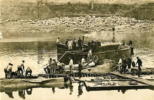 El sumergible, muy dañado, yacía en el puerto sobre un lecho de barro. Antes de que los hombres puedan entrar para extraer los cadáveres, una lancha de bombeo evacua el agua que la ha invadido © Dominio Magali