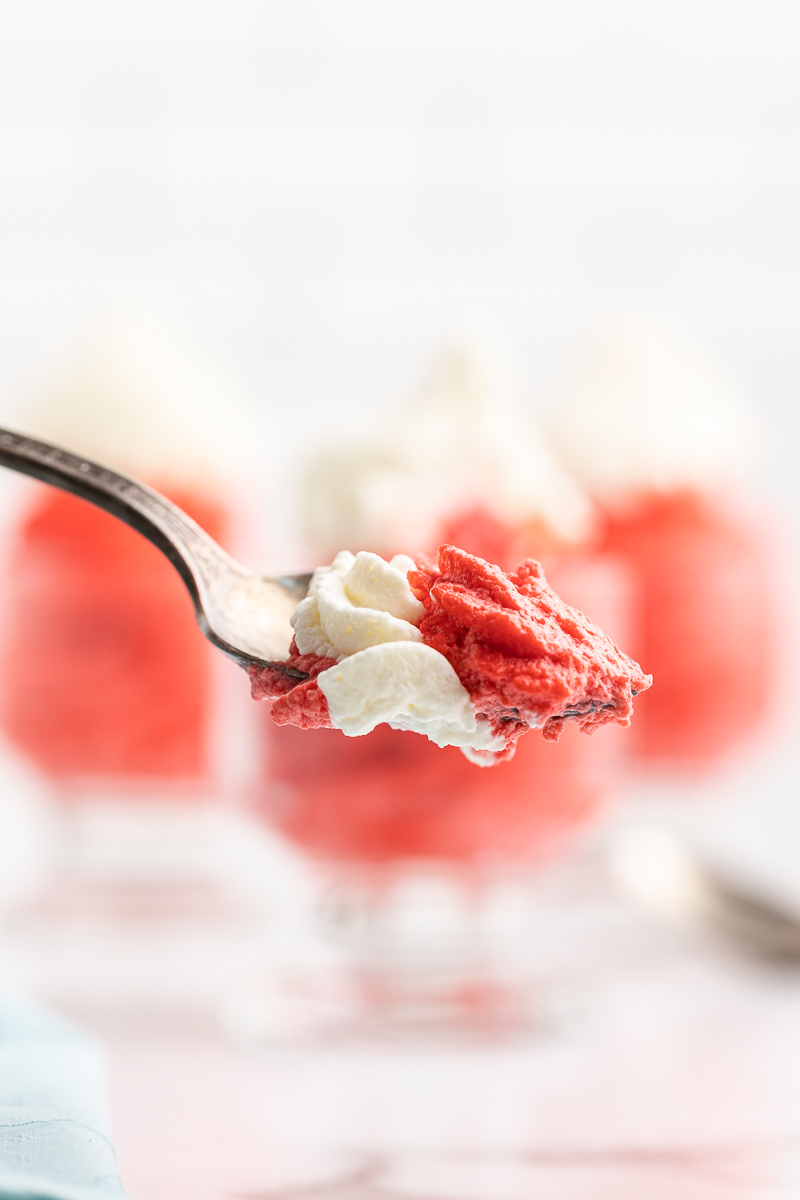 A spoonful of Keto Red Velvet Mousse close to the camera with the 3 glass dessert cups blurred in the background.