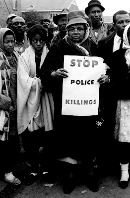 African - American woman holding a sign that says "Stop Police Killings" during the Selma March in 1965