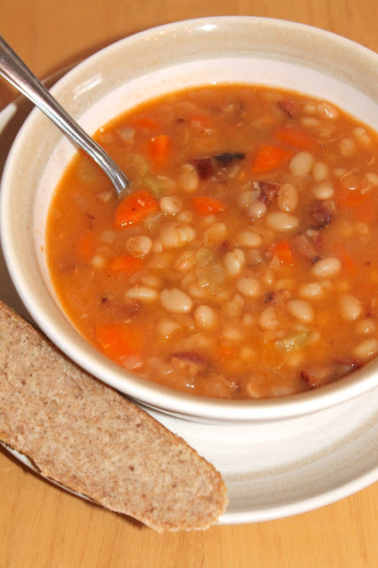 Bowl of bean with bacon soup with a side of bread.