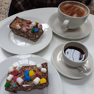 Two cups of coffee and two portions of rocky road cake with bright sweets