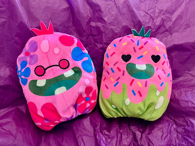 2 pink pickle plush. Groovy Gill has flowers on and pink glasses, Frosted Flow is covered in pink icing and sprinkles