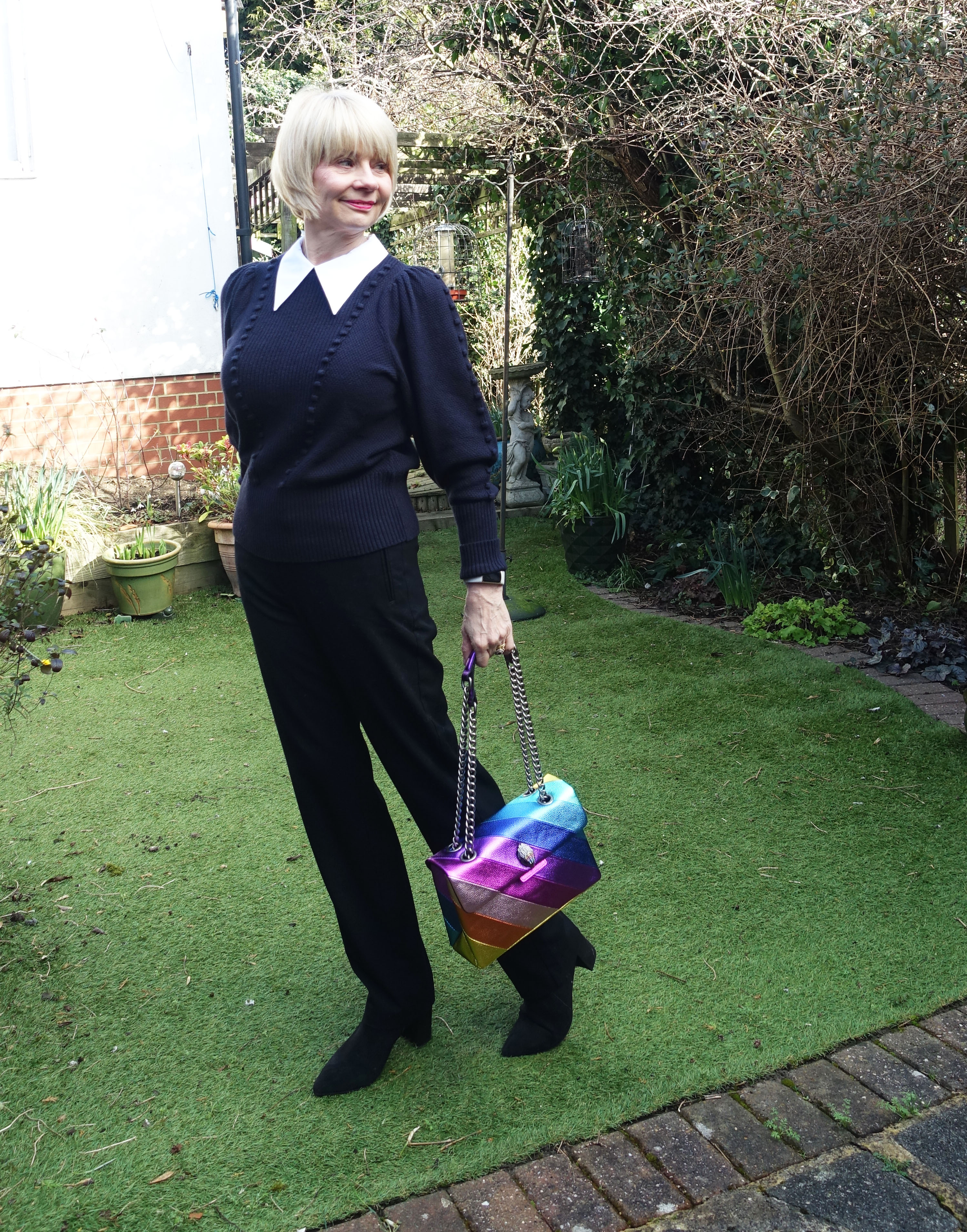 A Kurt Geiger rainbow bag adds colour to a black and white outfit worn by style blogger over 50 Gail Hanlon