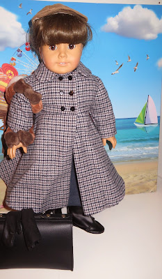 Girl doll in tan baseball cap and gray and white tweed coat holds plush monkey in front of backdrop of blue sky, beach, Ferris Wheel, sailboats