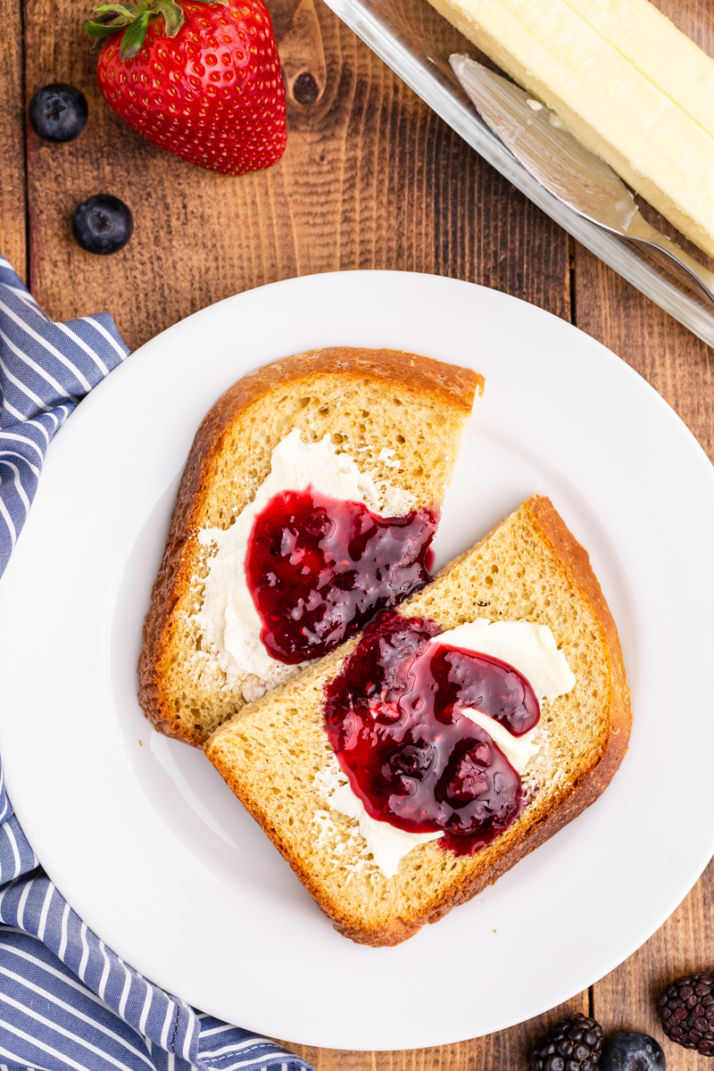 A slice of keto toast with butter and Keto Mixed Berry Jam on a white plate.