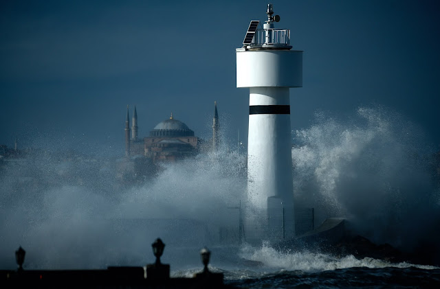 fırtınalı bir havada kdıköydeki deniz fenerini vuran dalgalar arasından ayasofya camine bir bakışın olduğu fotoğraf karesi.