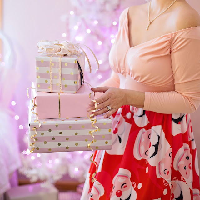 A person (head out of frame) carrying Christmas presents wrapped in pink and gold wrappers.