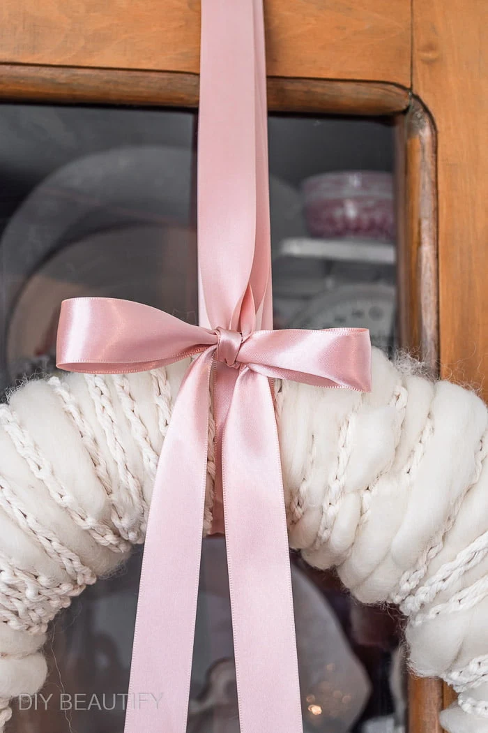 neutral winter cozy wreath hanging from pink ribbon