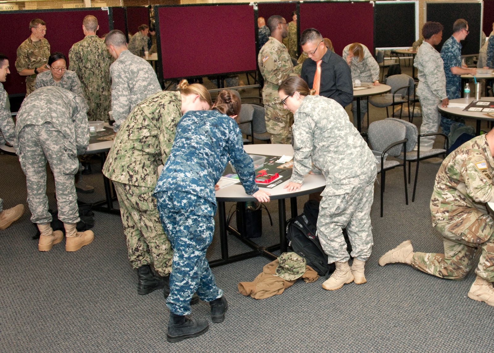 Fourth-year military medical students gather around several tables with game pieces and boards. They discuss and write things down.