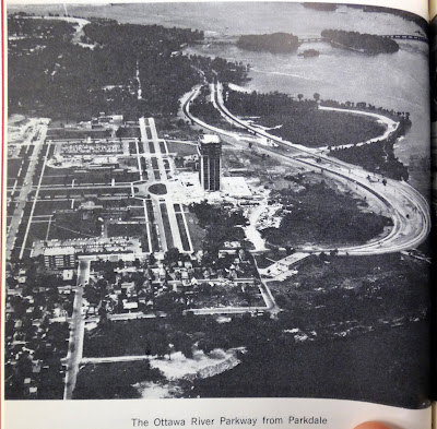 Black and white aerial photo looking west over Tunney's Pasture with the Ottawa River Parkway under construction westbound only from the north end of Tunney's Pasture.