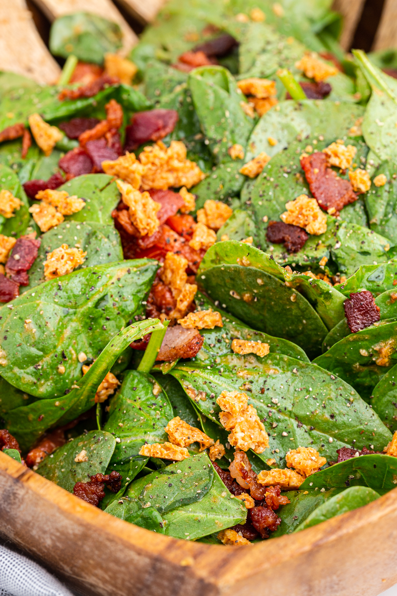 Close up of Spinach Salad with Hot Bacon and Tomato Vinaigrette in a wooden salad bowl.