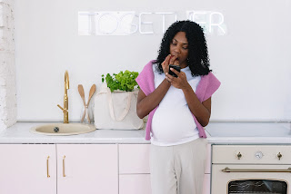 Pregnant woman looking at phone in kitchen in front of sign that says together