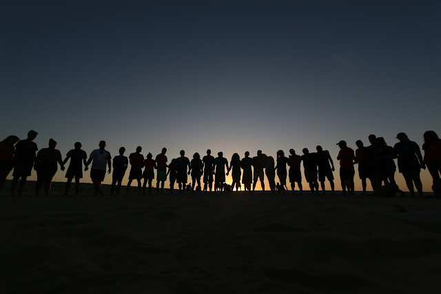 Persone in fila su una spiaggia in controluce al tramonto