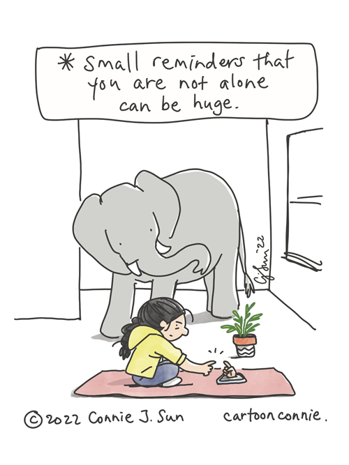 Single-panel comic of a girl with a braid at home, seated on a yoga mat, connecting with a friend on the phone. This is represented by a hand reaching out from a phone screen, index finger extended. The girl meets the hand halfway, fingertips about connect. Elephant looks on in the background. Caption reads, "Small reminders that you are not alone can be huge." Original cartoon illustration by Connie Sun, cartoonconnie, 2022