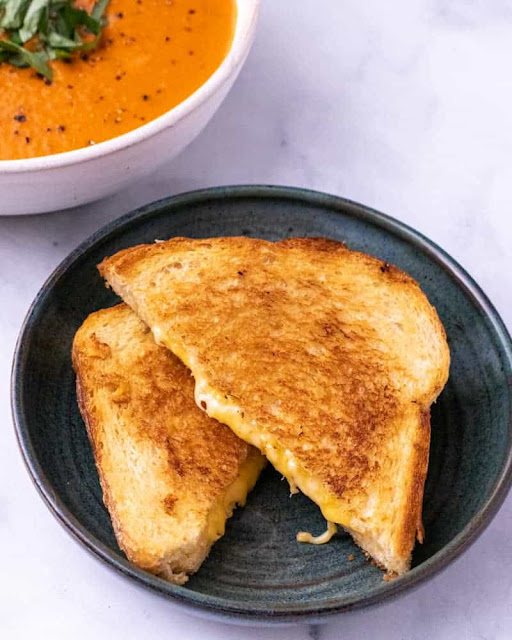 grilled cheese cut on a plate with soup in a white bowl.