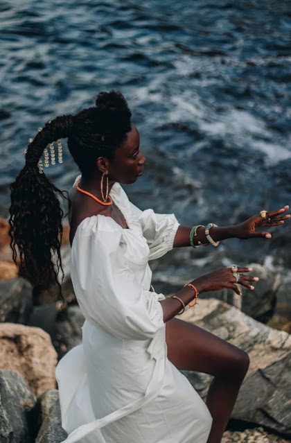 a imagem mostra uma mulher negra na praia com um vestido branco.